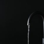 Closeup view of water flowing from faucet on black background. S