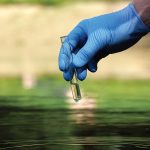 Hand in glove holding a test tube of clear water