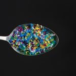 Microplastic in spoon on black background . Threat to human health and environment Dangerous additives Toxic substances.